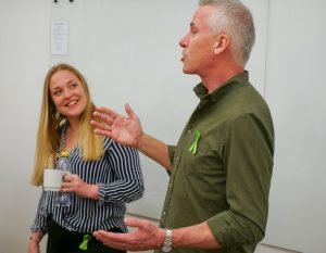 A photo of 2 people, the person on the right is speaking with their hands out in expression, and the second person is looking at them, smiling.