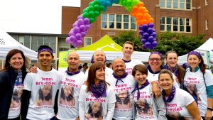 A group photo of the Team Easy Bre-ezies, with a big rainbow balloon arch behind them.