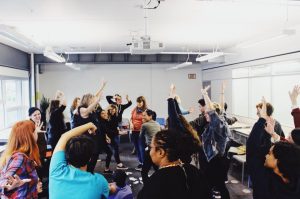 A photo of Stella's Place staff doing a group stretch with arms raised high in the air.