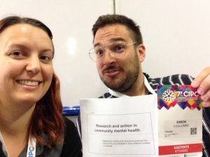 A selfie of Steph & Simon smiling and holding up papers.