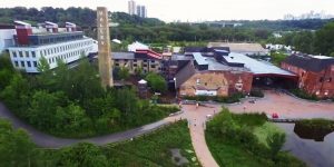 An aerial shot of the Toronto Brickworks building, taken in the summer with lush greenery surrounding the building. You can see a bit of the city skyline off in the distance.
