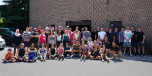 A group photo of dozens of people all dressed in workout clothes. The photo was taken outside in a parking lot, with a brick building behind them.