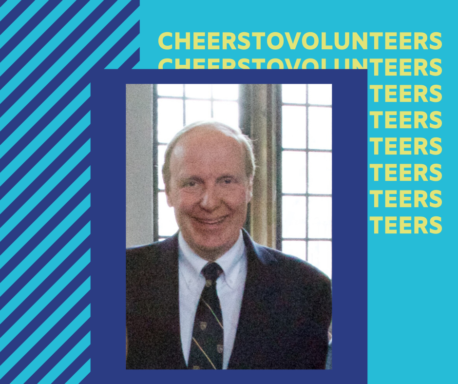 A portrait of Geoff wearing a black suit and tie. The image has a purple border around and is in the middle of a blue graphic with text repeated and obstructed behind the photo that reads "Cheers to volunteers"