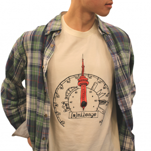 Photo of person from the neck down wearing white t-shirt with graphic of speedometer illustrated with Toronto buildings around and a red CN tower. Reads [Smile]age in black below