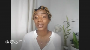 A screenshot from a video on CBC News featuring Lereen. Lereen, pictured here is mid speech, with short hair and gold eye shadow, earing a white longsleeve shirt. Behind her is a white wall with a green plant in the background. In the bottom left corner is the CBC News logo.
