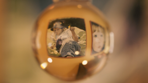 A photo with a warm yellow hue looking through a glass ball to a painting of a child, which makes the painting look distorted through the glass.