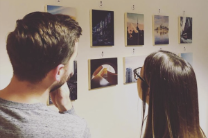 A photo of the back of 2 people who are looking at photos hung up on a gallery wall.