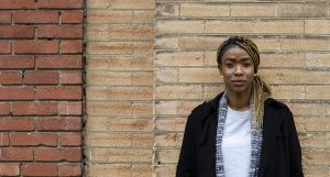 Photo of a young adult standing in front of a light brown brick wall