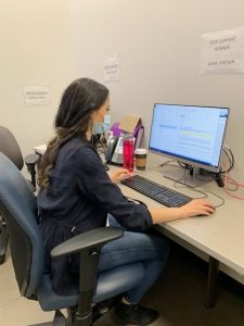 Yolanda sitting at a computer. There's a sign above the monitor that reads "Peer Worker Work Station"