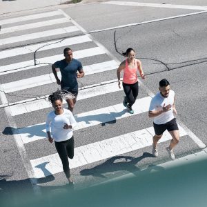 An overhead view of 4 people jogging across a walkway on a paved street.