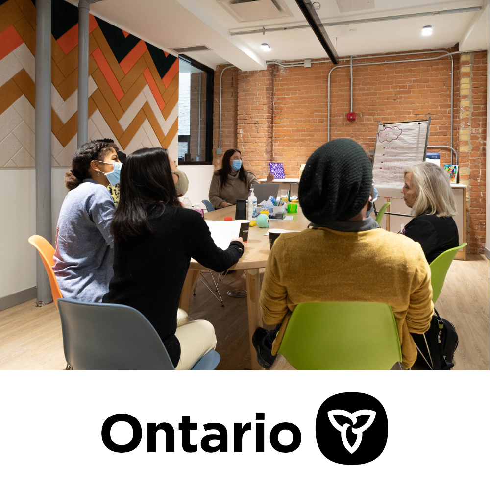 A group of people sit in a room having a meeting, with the Ontario Newsroom logo below
